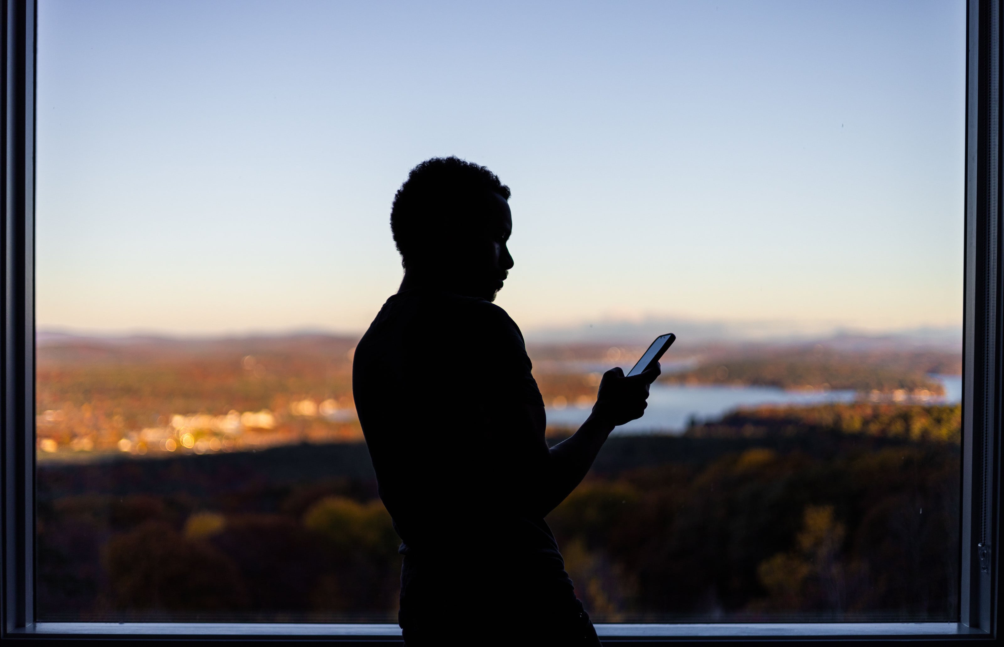Persona a contraluz mirando su celular frente a una ventana con vista a las montañas