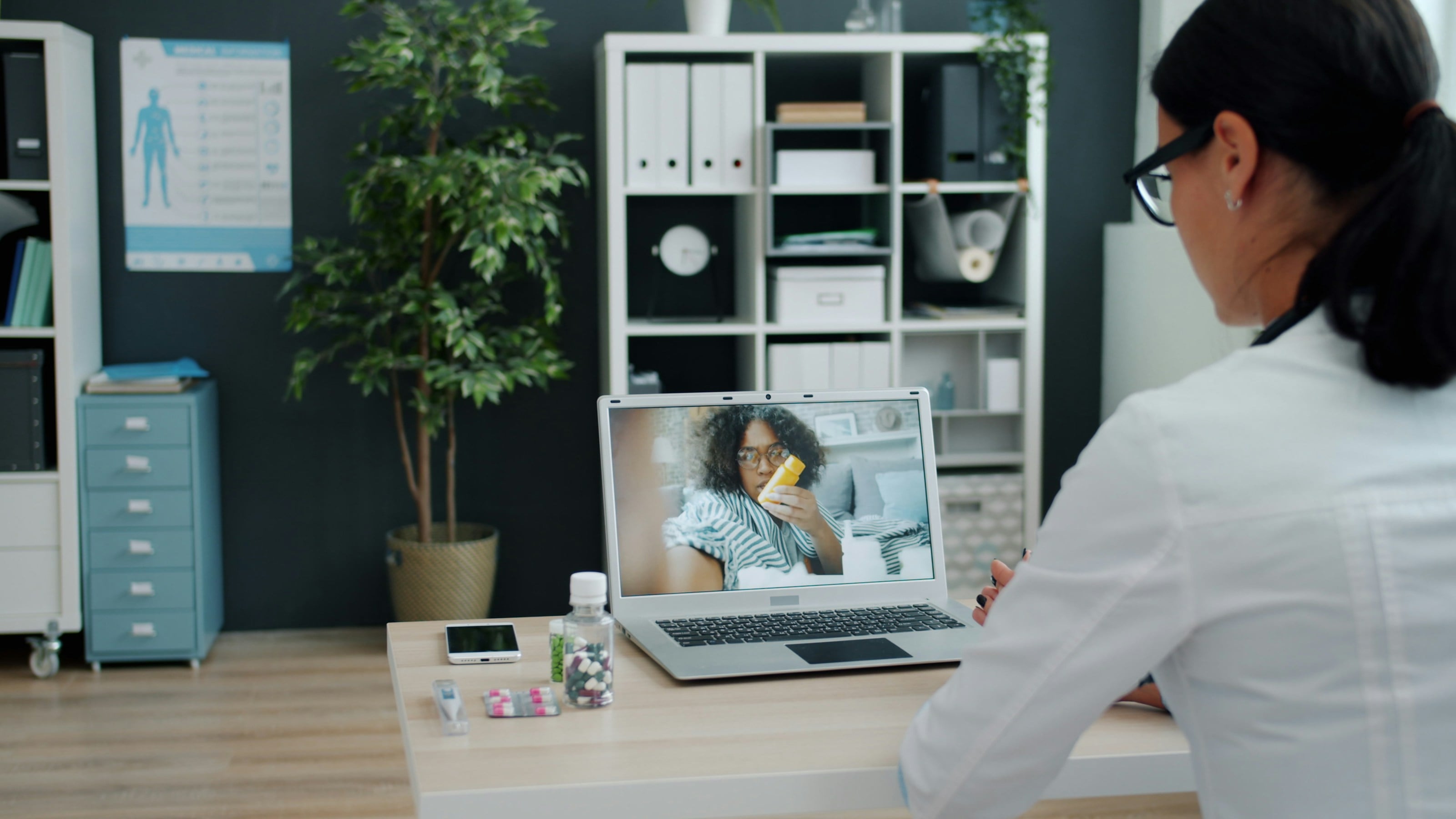 Médica atendiendo por videollamada a una paciente que aparece en la pantalla del portátil